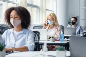 Company employees work in office. Multiracial managers in protective masks at workplaces with